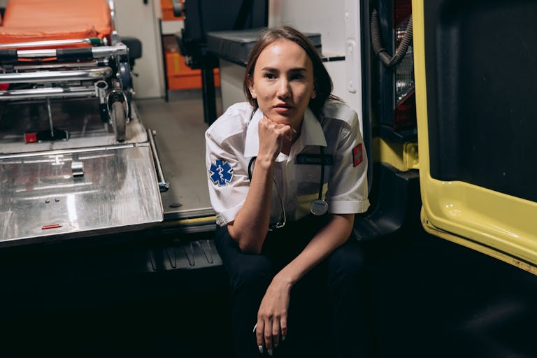 A female paramedic in uniform sits thoughtfully inside an ambulance, showcasing emergency readiness.