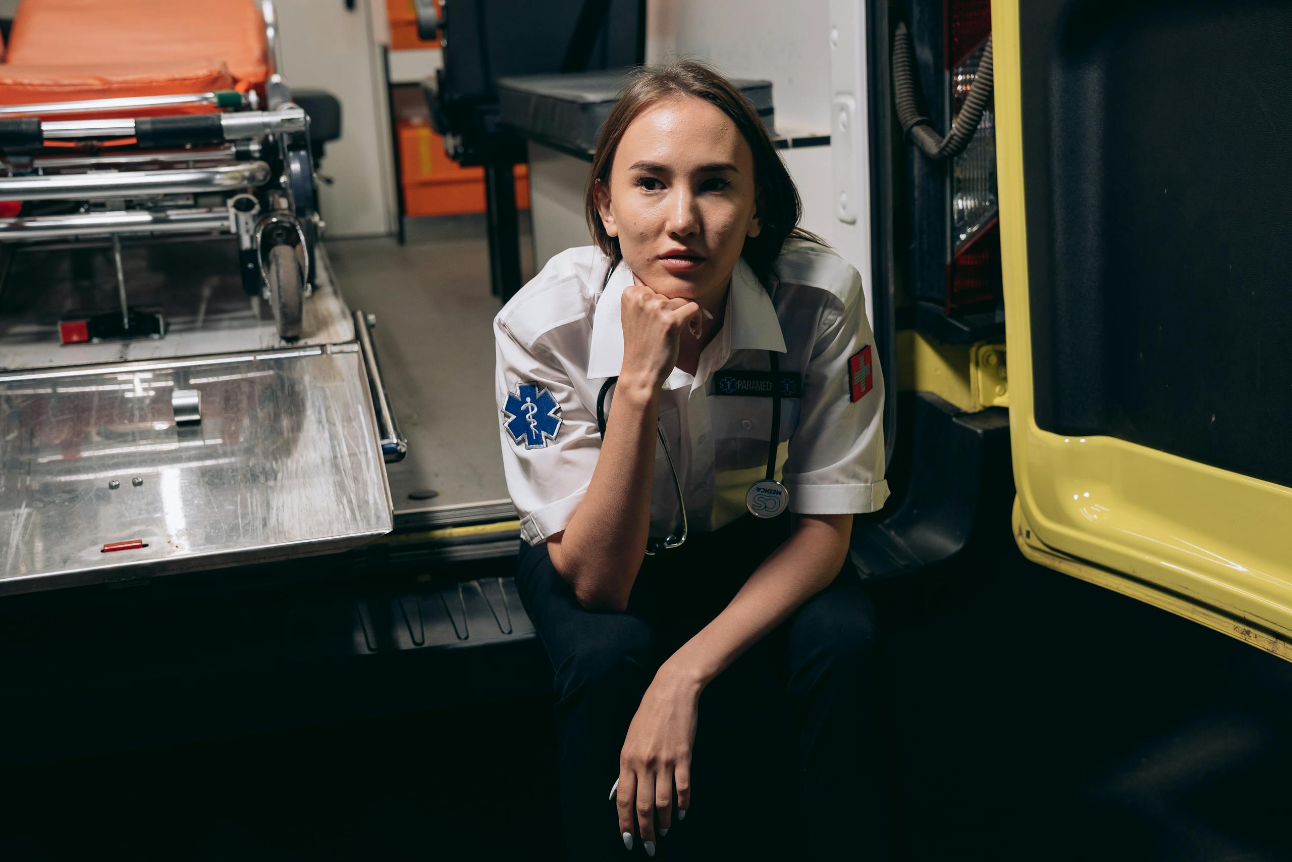 A female paramedic in uniform sits thoughtfully inside an ambulance, showcasing emergency readiness.
