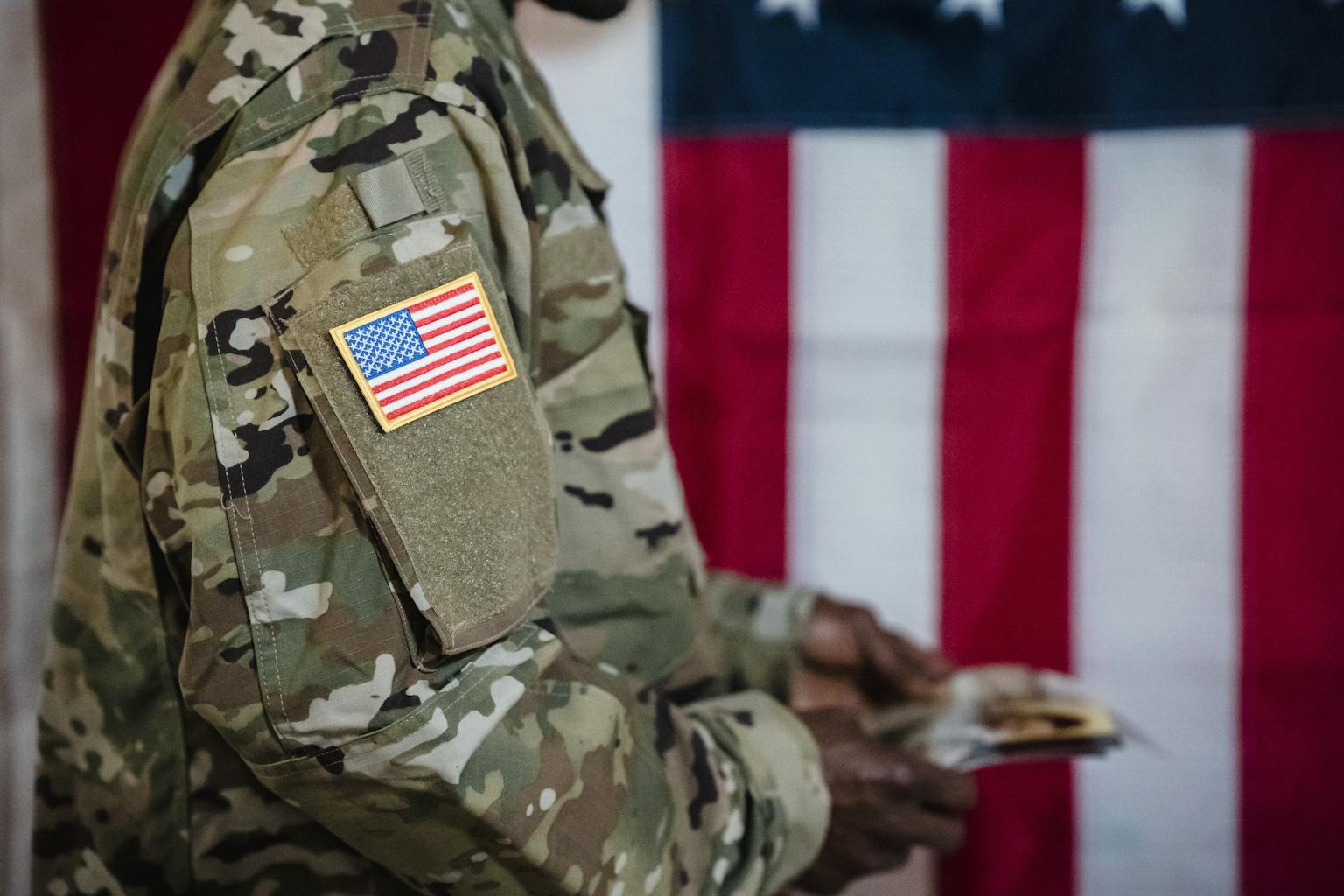 Close-up of a soldier in military uniform with American flag patch and background.