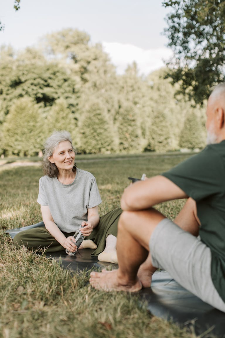 Elderly couple practicing yoga in a sunny park setting, promoting wellness and relaxation.